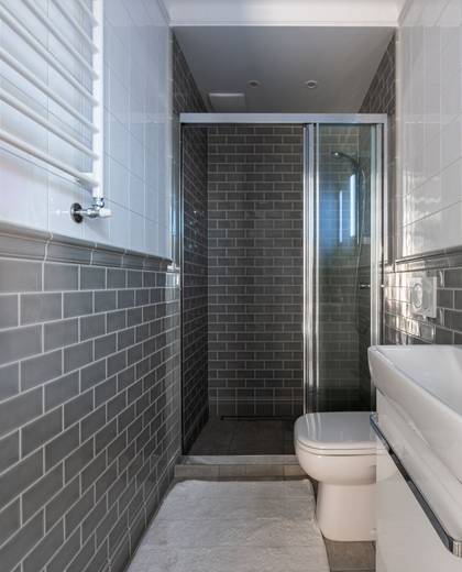 A freshly finished bathroom with grey brick-effect tiles and a glass shower